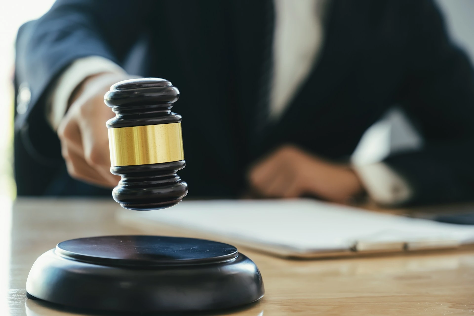 A judge holding a wooden gavel above a sound block at a desk.